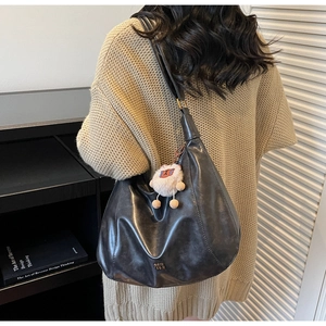 Detail of dark matte leather hobo bag with metal logo and plush charm on shoulder