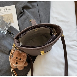 Détail du sac seau en cuir marron foncé avec fermeture éclair et breloque ours
