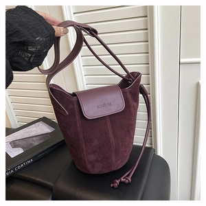 Detail of burgundy suede bucket bag with adjustable strap on a black cushion
