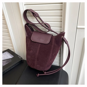 Detail of burgundy suede bucket bag showing contrast leather flap and debossed logo