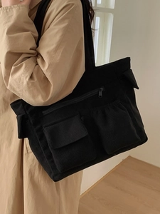 Black corduroy tote bag with multiple pockets worn by a model over a beige coat