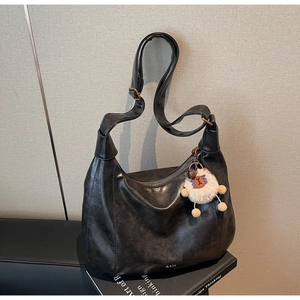 Detail of black soft leather tote bag featuring adjustable strap and white sheep pendant