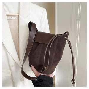 Close-up of matte suede texture and embossed logo detail on the dark brown bucket bag