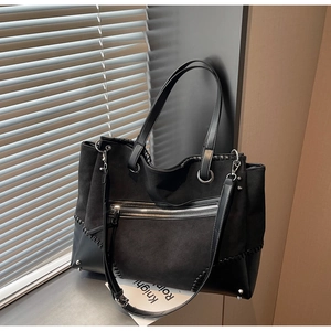 Detail of black tote bag with woven stitching, silver rivets and front zipper pocket