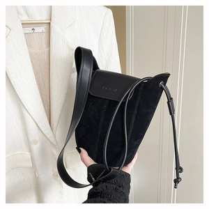 Detail of black suede bucket bag featuring embossed logo and contrast leather flap
