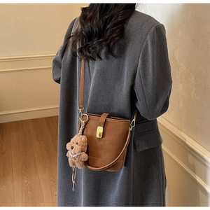Sac seau en cuir marron avec boucle dorée et breloque ours sur un manteau en tweed gris