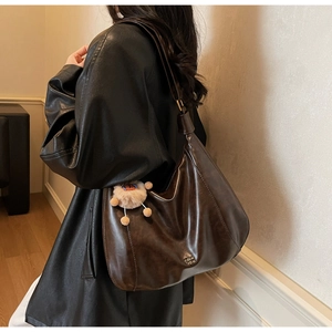 Detail of dark brown vintage leather tote bag with metal logo and plush keychain accessory