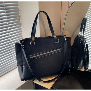 Detail of black tote bag showing stitching, front zip pocket and bottom metal rivets