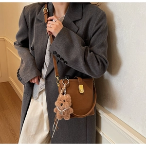 Détail du sac seau en cuir marron avec boucle dorée et breloque d'ours en peluche