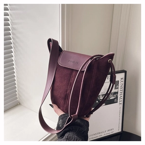 Detail of burgundy suede bucket bag featuring a magnetic flap and decorative drawstring