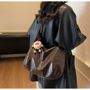 Detail of dark brown leather tote bag with metal logo and plush animal charm