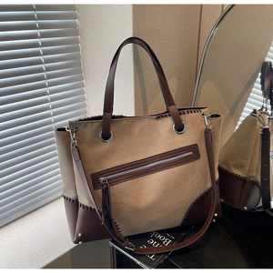 Detailed stitching on two-tone tote bag with brown leather trim and metal feet rivets