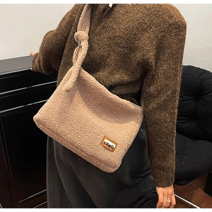 Detail of beige fleece crossbody bag featuring a leather logo patch and knotted shoulder strap