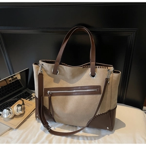 Detail of canvas tote bag with brown leather trim and woven stitching on a white table