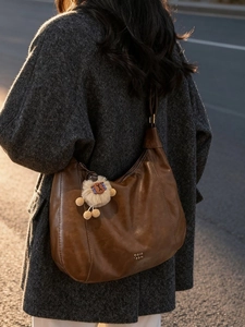 Brown leather hobo tote bag with lion plush charm shown from a side-view on a model