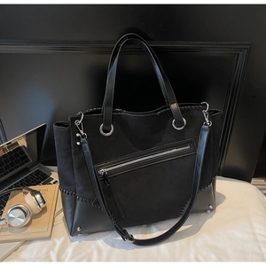 Close-up of black tote bag featuring matte fabric, leather patches, and metallic stud details