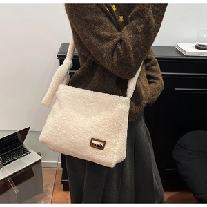 Detail of plush faux shearling shoulder bag with brown leather brand tag on beige texture