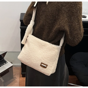 Detail of white plush shoulder bag featuring a brown leather logo patch on fuzzy texture