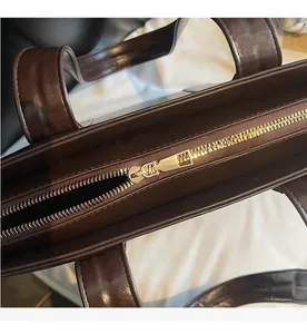 Gros plan d'une fermeture éclair en métal doré sur un sac cabas en cuir marron foncé