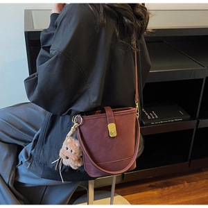 Détail du sac seau bordeaux avec garniture dorée et charm de chiot en peluche sur la lanière