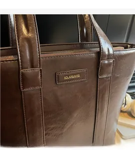 Détail d'un cabas en cuir marron foncé montrant le logo doré et la texture lisse