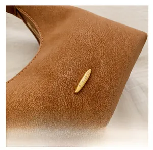 Detail of brown pebbled leather bag with gold hardware and logo-engraved metal accent
