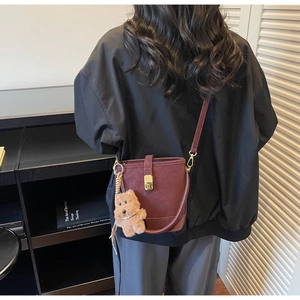 Mannequin portant un sac seau rétro bordeaux avec charm ours en peluche au style urbain