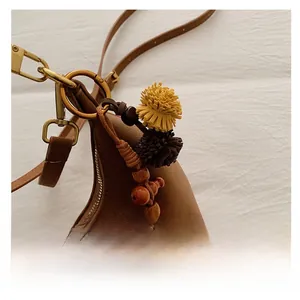 Detail shot of brown crescent bag featuring plush pom-poms and wooden bead charms