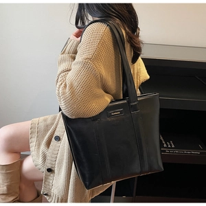 Détail du grand cabas noir en cuir brillant avec logo doré sur un cardigan beige