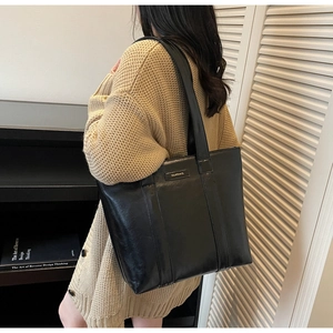 Gros plan d'un sac cabas noir en cuir brillant avec une large bandoulière et grand volume