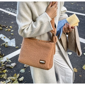 Detailed close-up of brown teddy plush crossbody bag with leather logo patch on street
