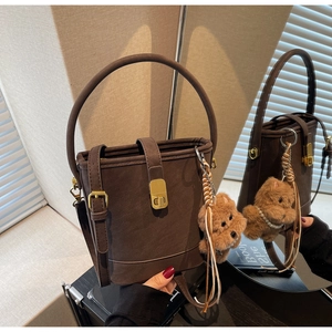 Detail of dark brown bucket bag with gold clasp and cute teddy bear charm hanging on the side