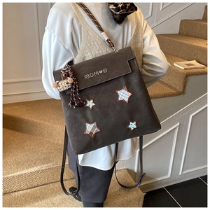 Détail d'un sac à dos mat marron foncé avec écussons étoiles et breloque ours en peluche