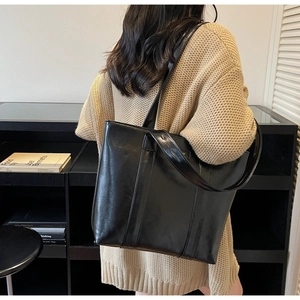 Grand sac cabas noir élégant en cuir brillant porté par un mannequin en tenue chic