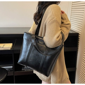 Détail du sac cabas en cuir noir brillant avec plaque logo métallique et longue bandoulière