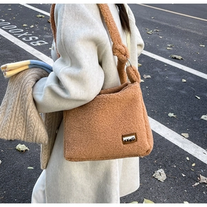 Close-up of caramel fleece crossbody bag with TXBD leather patch on white coat model