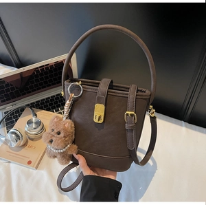 Détail du sac seau marron café avec boucle dorée et breloque de chien en peluche mignonne