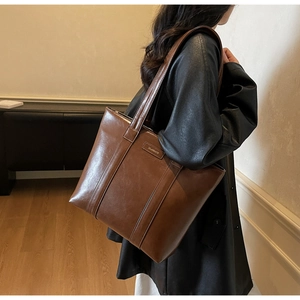 Détail d'un sac cabas en cuir marron vintage avec écusson logo porté par un mannequin