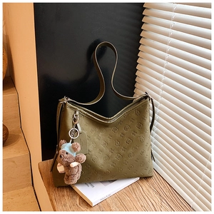 Close-up of moss green tote bag with embossed floral patterns and a cute brown bear charm