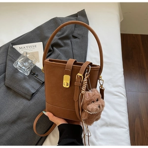 Détail du sac seau en cuir mat marron avec fermoir doré et breloque chien en peluche sur lin