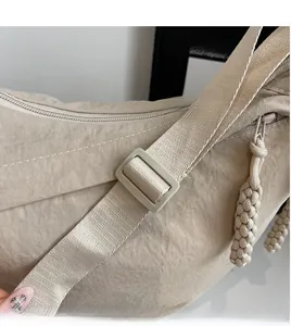 Detail view of beige nylon shoulder bag showing adjustable strap and smooth zipper pulls