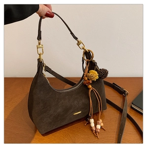 Detail of dark brown matte crescent bag with gold hardware and ethnic tassel pendant