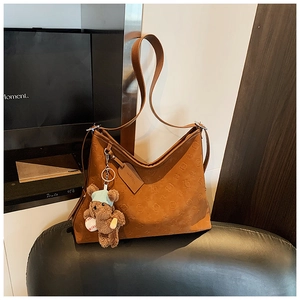 Detail of brown embossed leather shoulder bag featuring a cute teddy bear charm