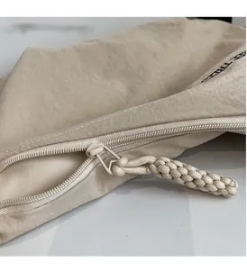 Detail of smooth metal zipper and woven puller on beige canvas crossbody dumpling bag