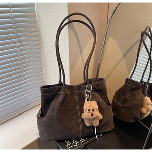 Detail of dark brown suede tote bag with white stitching and plush bear charm