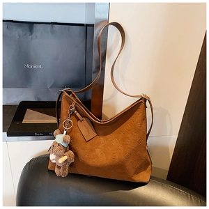 Detail of vintage brown tote bag with embossed logo texture and plush bear charm