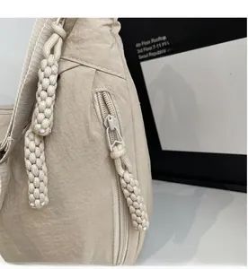 Detailed close-up of smooth zipper with woven cord puller on beige nylon crossbody bag