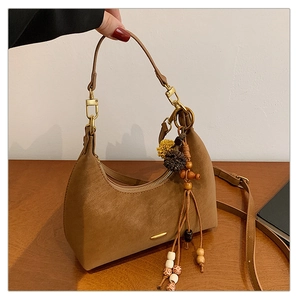 Detail of caramel suede hobo bag with ethnic style wooden beads and fluffy ball charm