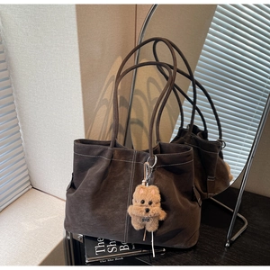Detail of brown suede tote bag with white contrast stitching and plush dog charm