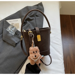 Détail du sac seau en cuir marron foncé avec fermoir doré et breloque ours en peluche